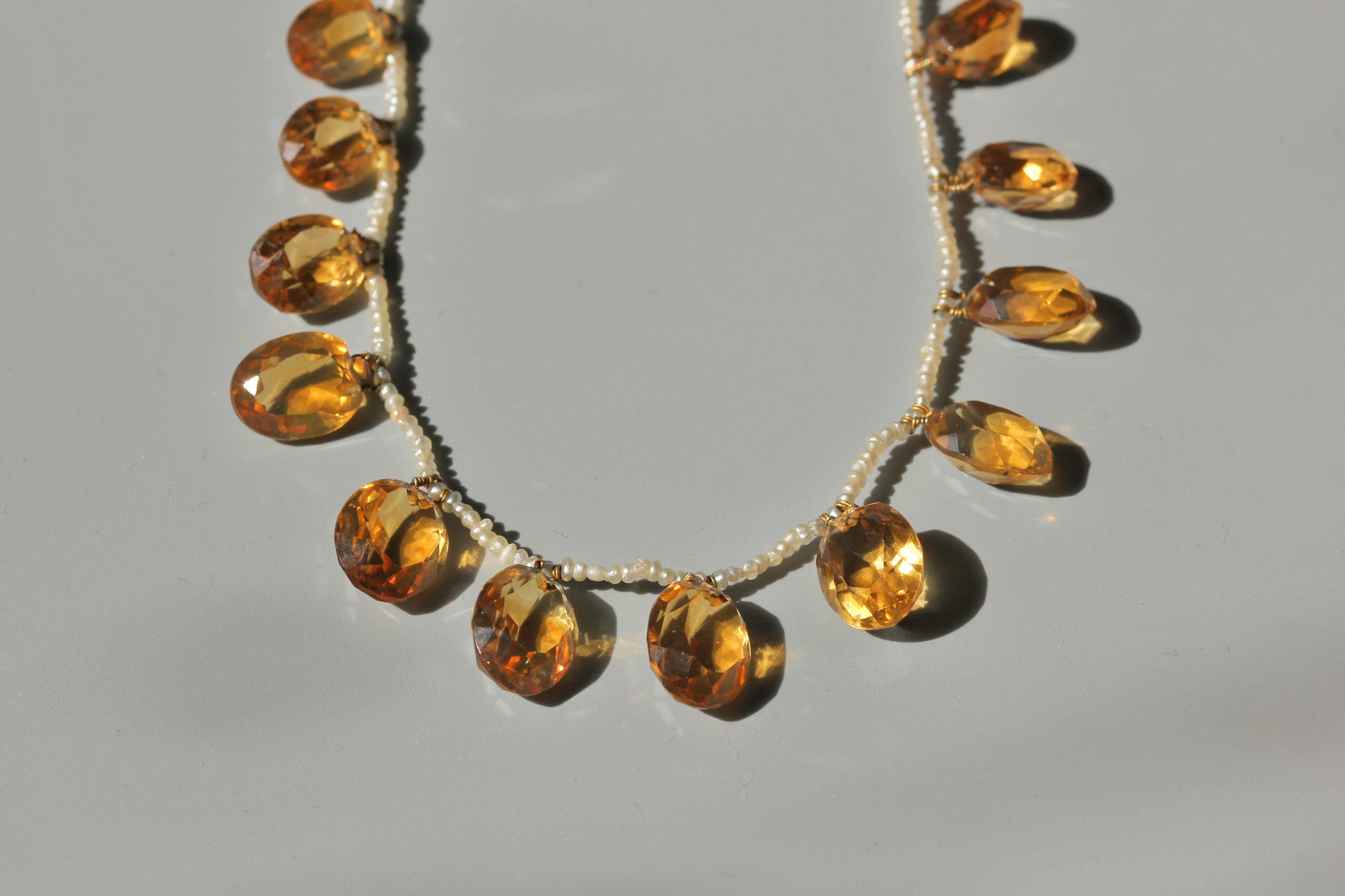Close up of faceted golden citrine drops and tiny seed pearls on antique fringe necklace