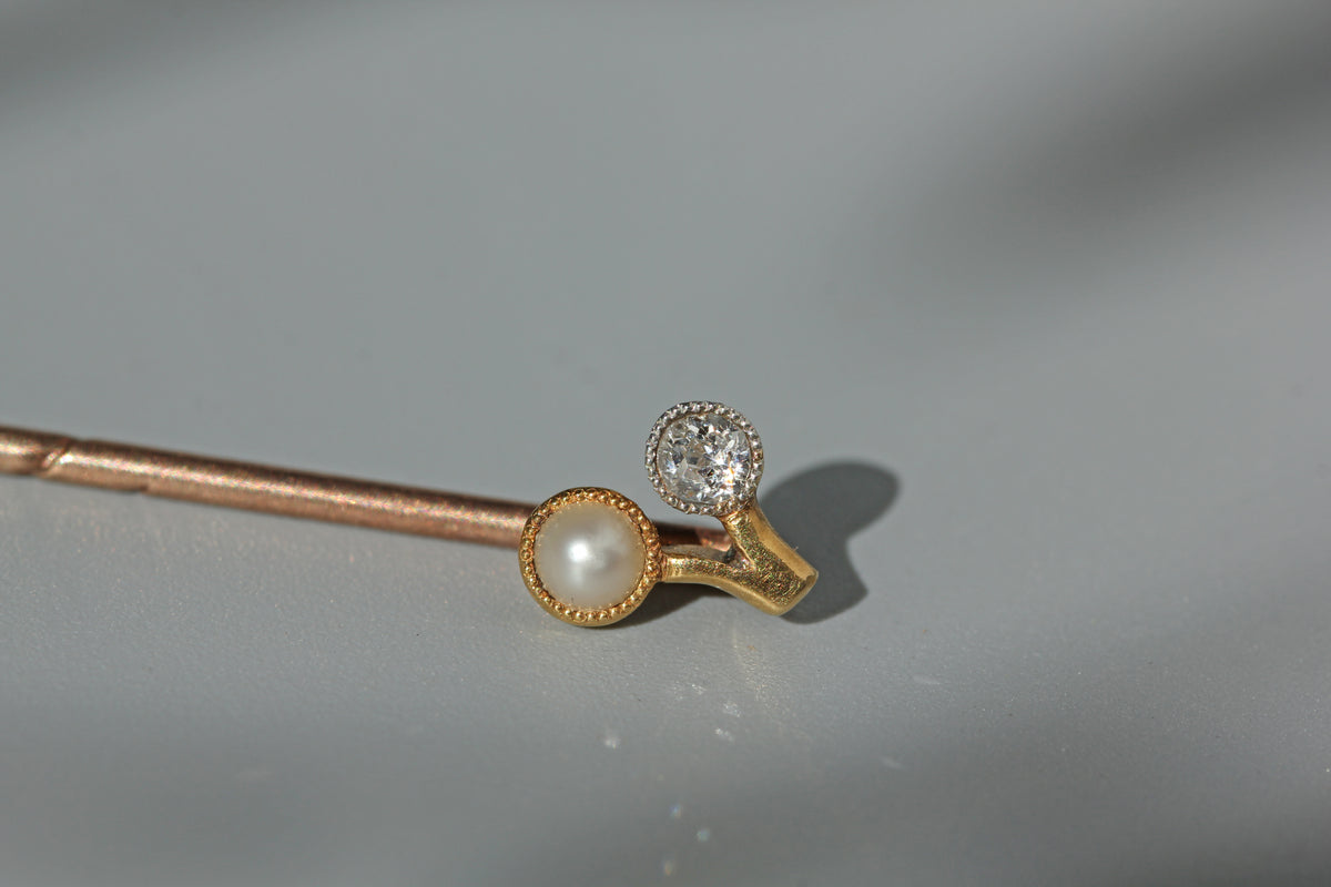Close up of pearl and old cut diamond stick pin with a cherry shaped mount, crafted in buttery 18ct gold and dating to the art deco era