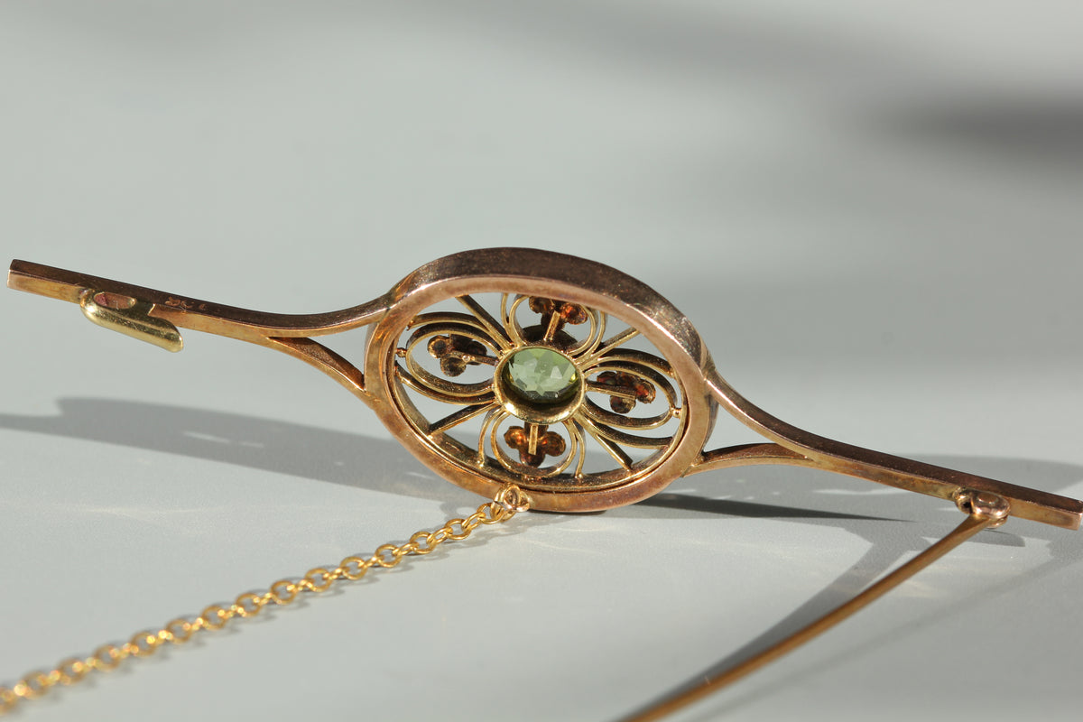 Detailed view of the back of an antique gold brooch with a peridot stone at the centre and the antique clasp details shown