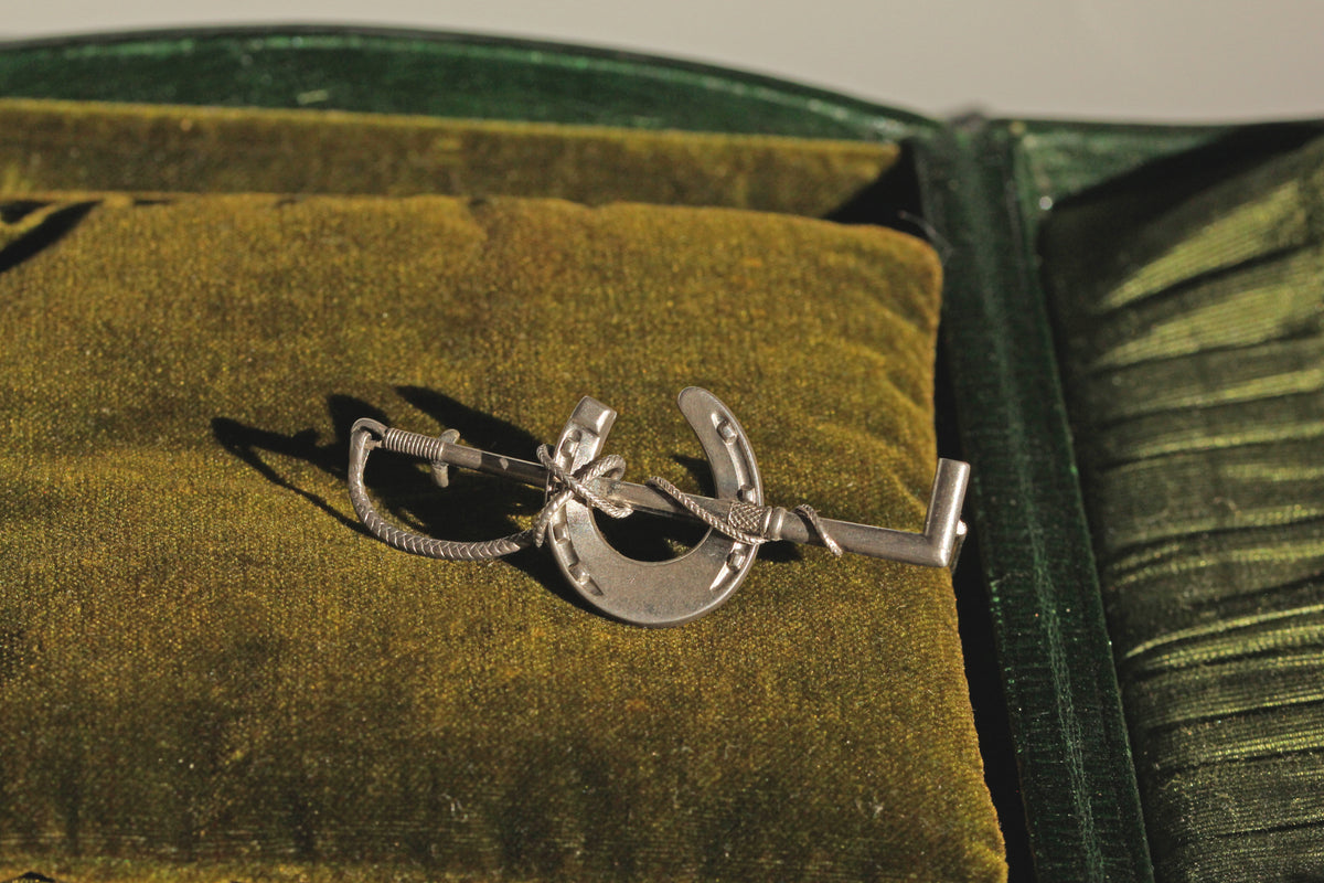 Antique sterling silver riding crop and horseshoe brooch with dramatic shadowing