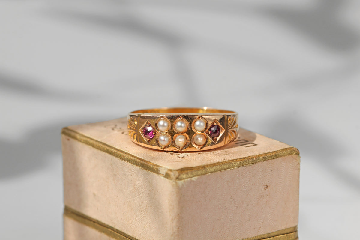 Antique victorian 15ct gold band ring decorated with rubies and pearls, displayed on vintage jewellery box