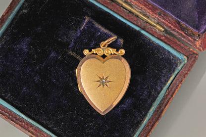 A vintage 9ct gold heart shaped locket pendant with a star motif in the centre set with a rose cut diamond, displayed inside an antique wooden box with a dark purple velvet lining.